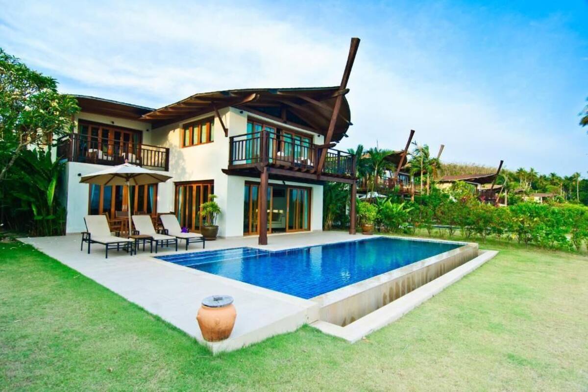 A two-story house with a swimming pool, outdoor furniture, and a large umbrella.