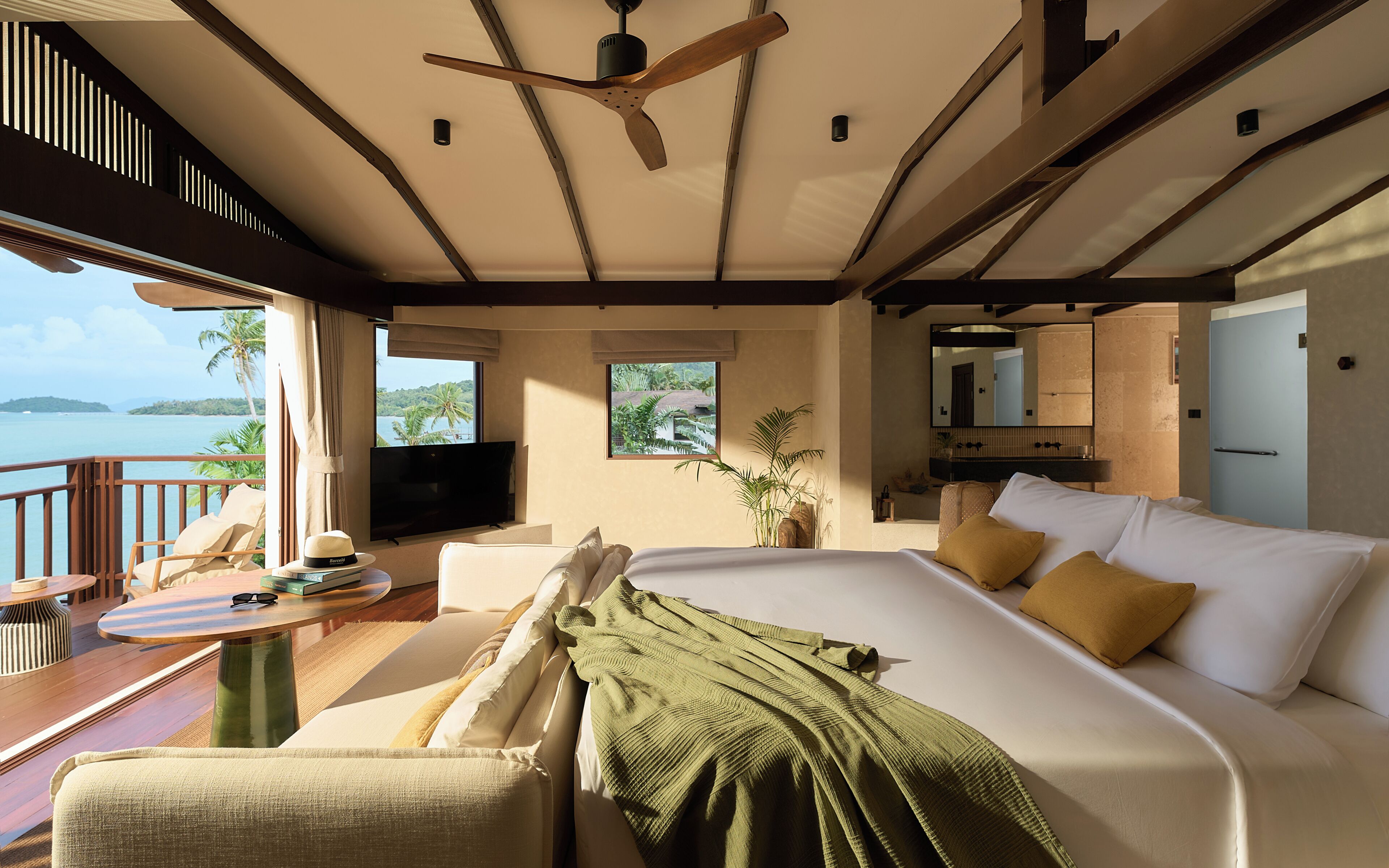A spacious bedroom with a large bed, a television, a balcony with a view of the sea, and a dining area.