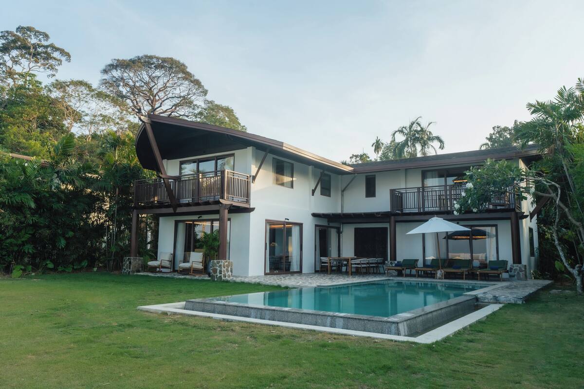 A two-story house with a swimming pool, outdoor seating, and a garden.
