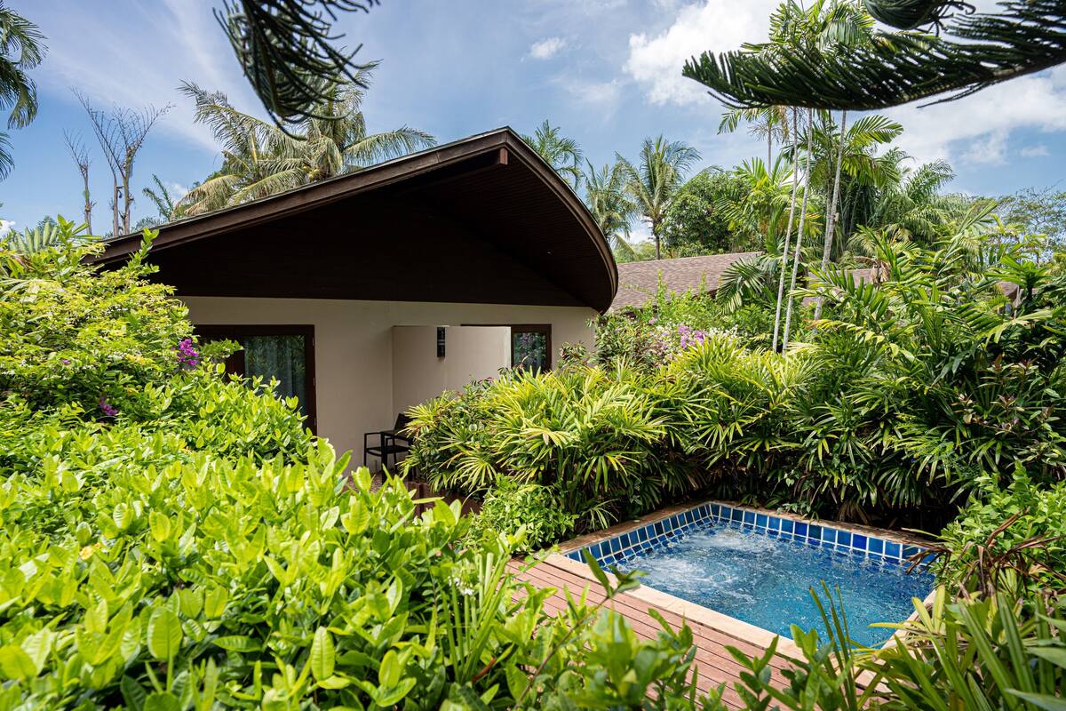 A pool surrounded by lush greenery and a small building with a sloped roof.