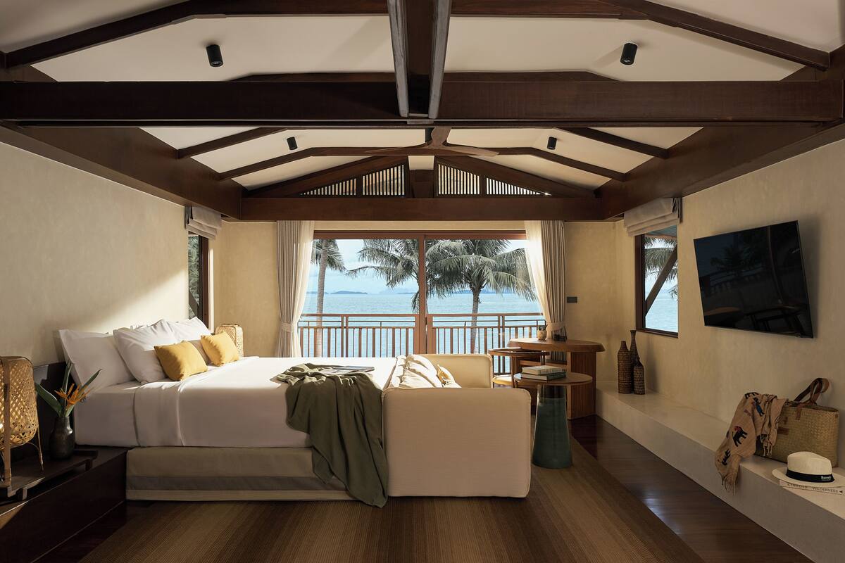 A spacious bedroom with a large bed, a view of the sea, and a balcony with a table and chairs.