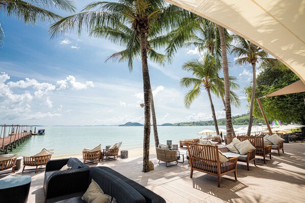 A deck with wicker furniture, a view of the sea, and palm trees.