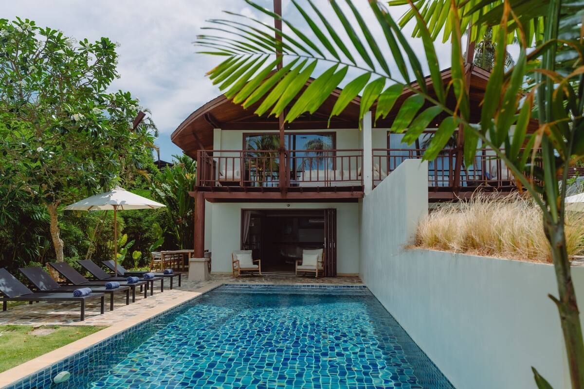 A pool area with lounge chairs and a two-story building with a balcony.
