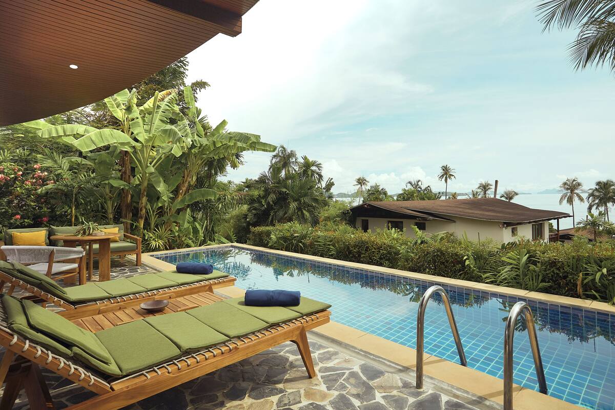A poolside area with lounge chairs, a table, and a view of the ocean.