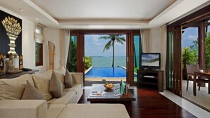 A spacious living room with a large sofa, a coffee table, and a television. There is a view of a swimming pool and the ocean through large glass doors. - Barcelo Coconut Island Phuket (Maprao Island)