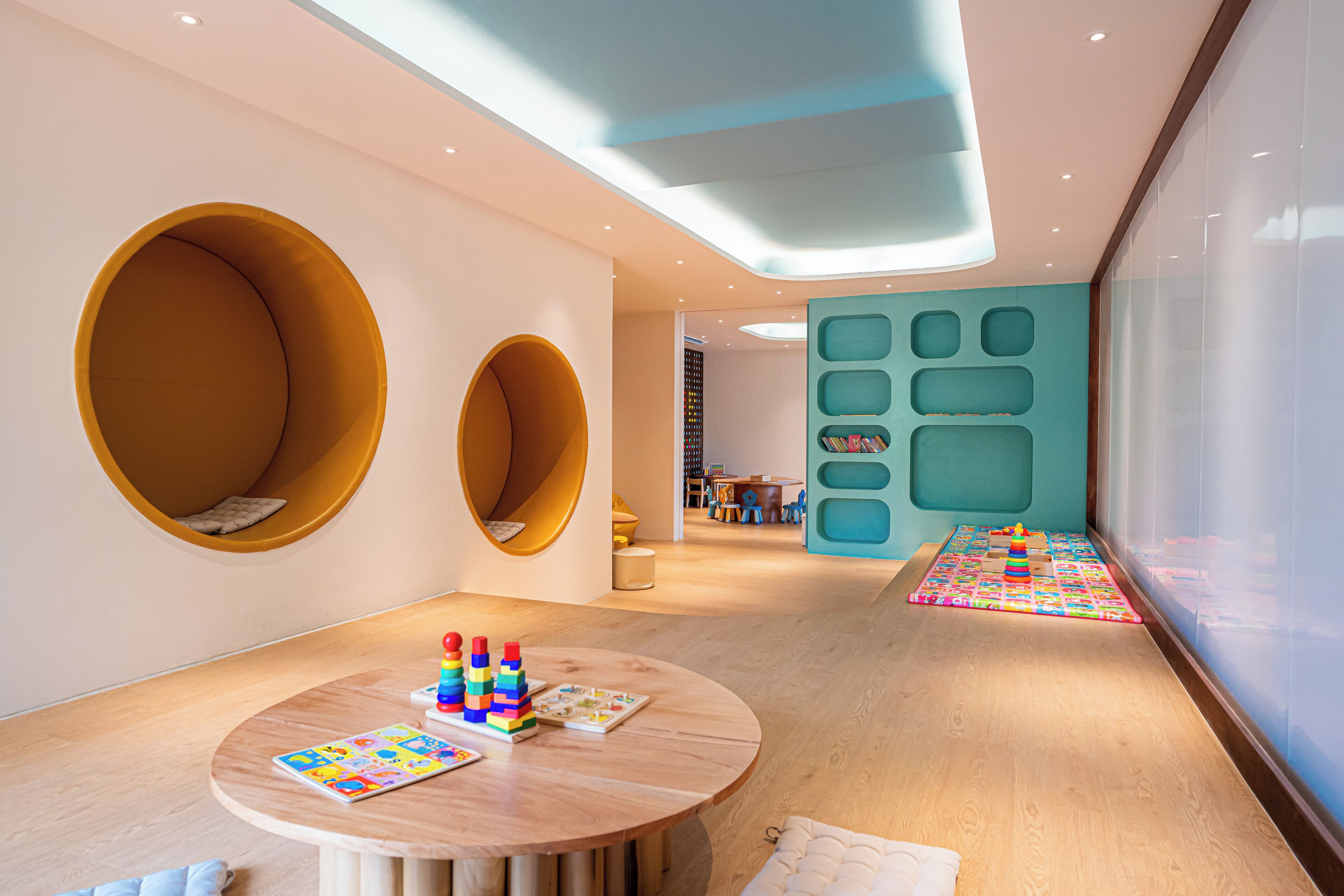 Een moderne kinderspeelruimte met ronde zitplaatsen, een speelmat en een boekenplank.