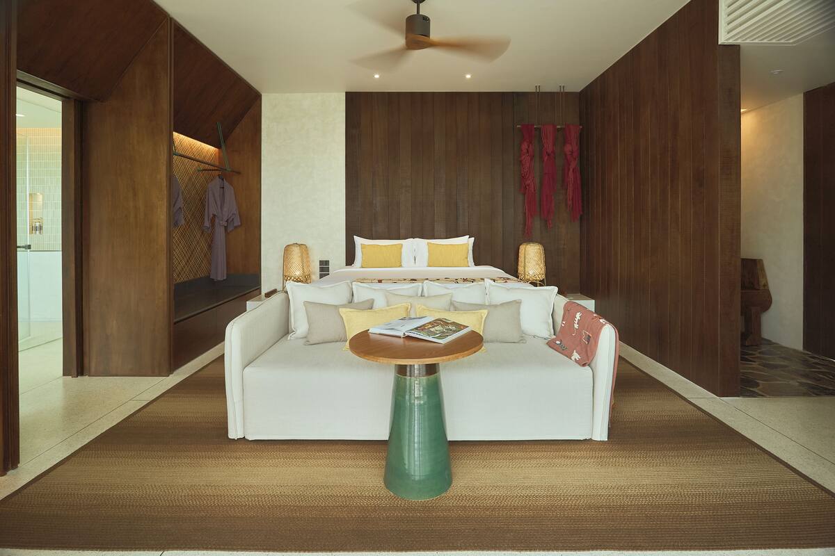 A modern hotel room with a bed, a white sofa, a round table, and a ceiling fan.