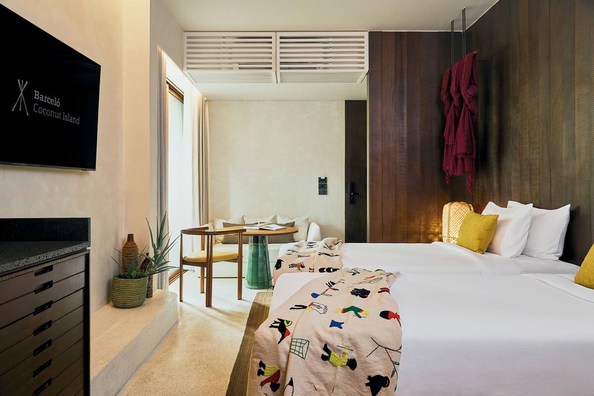 A hotel room with a bed, a desk, a chair, a TV, and a plant.