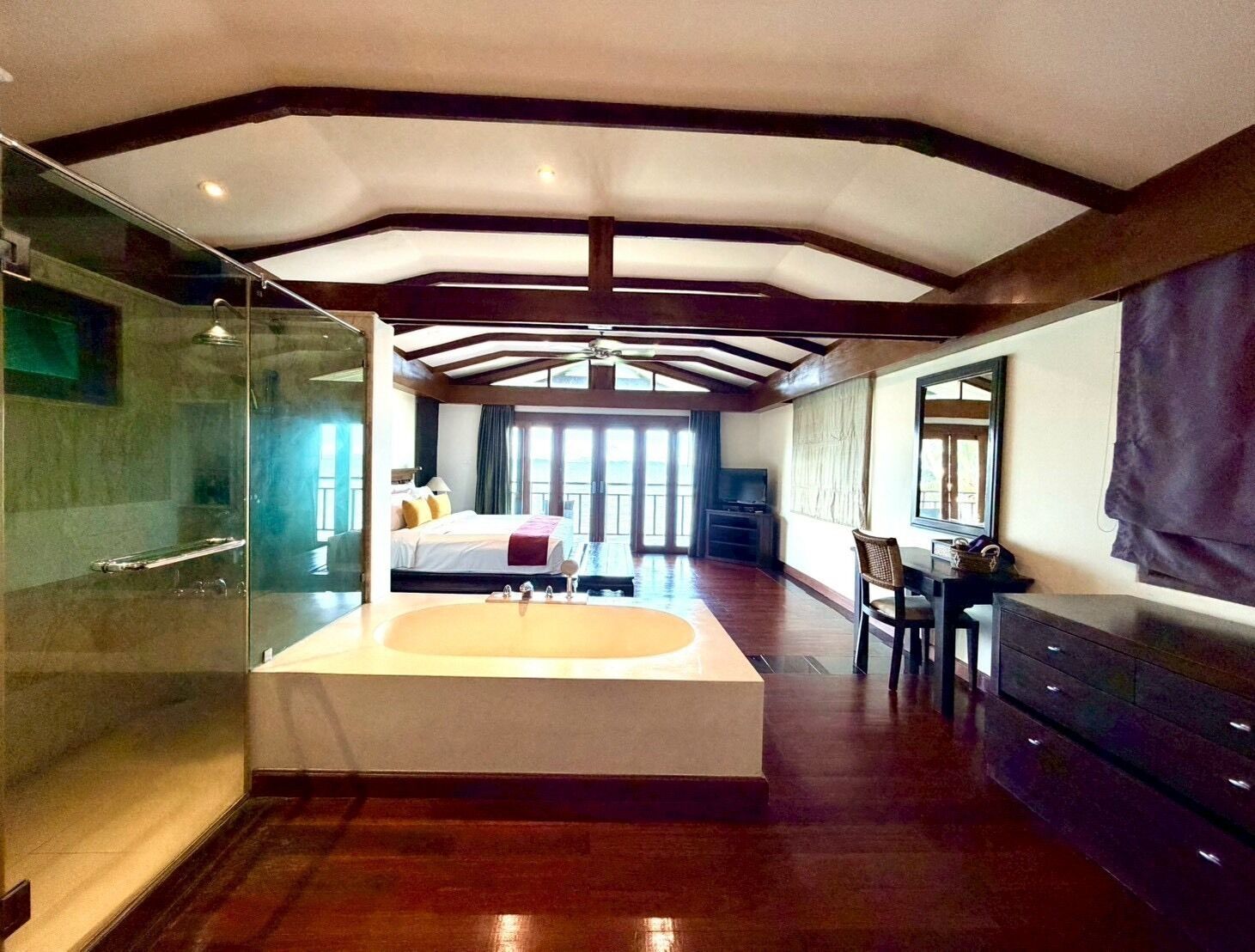A spacious bedroom with a large bed, a glass-enclosed shower, and a separate vanity area.