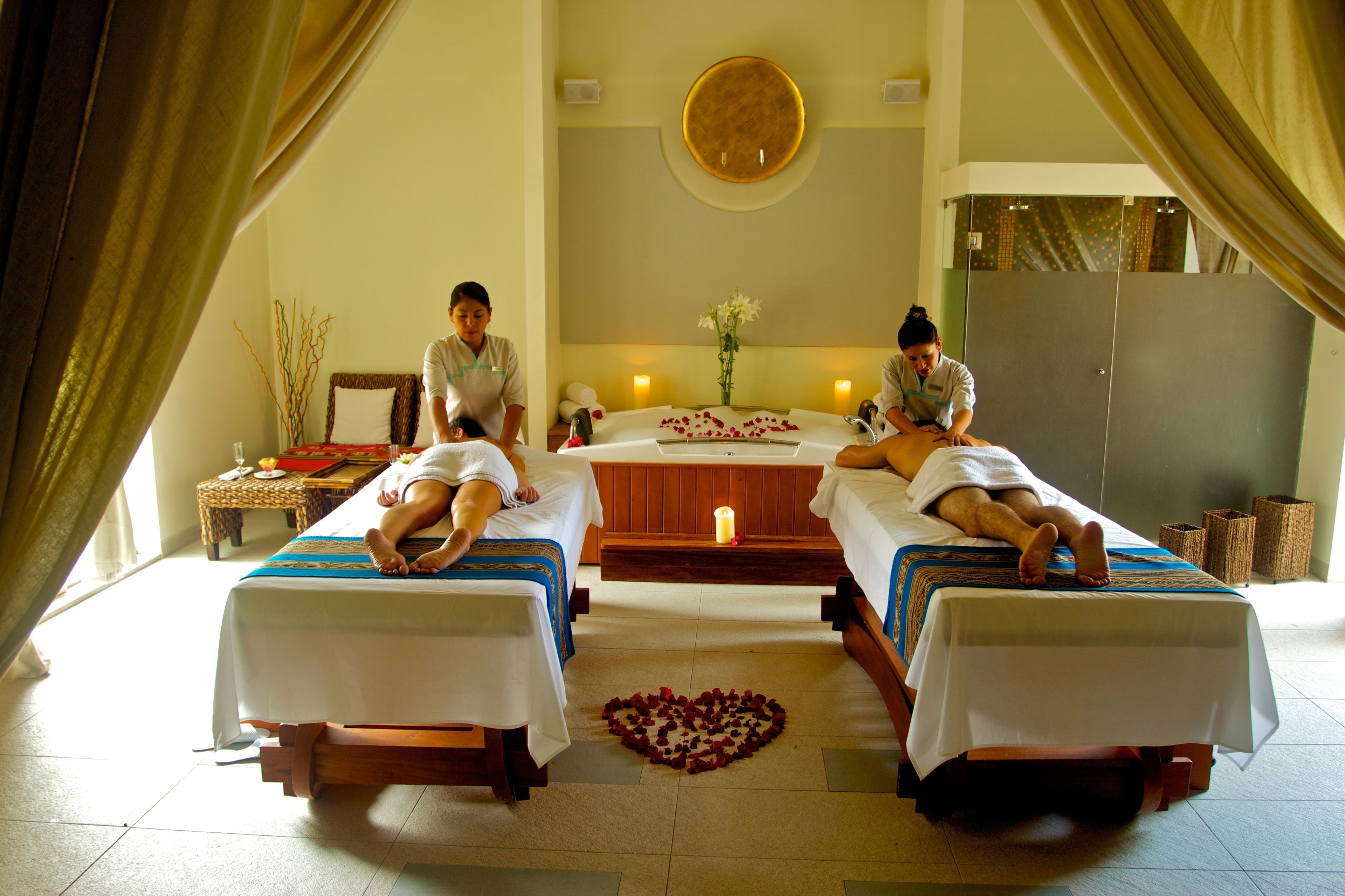 A spa room with two massage tables, a central massage table, and a small table with a vase of flowers.