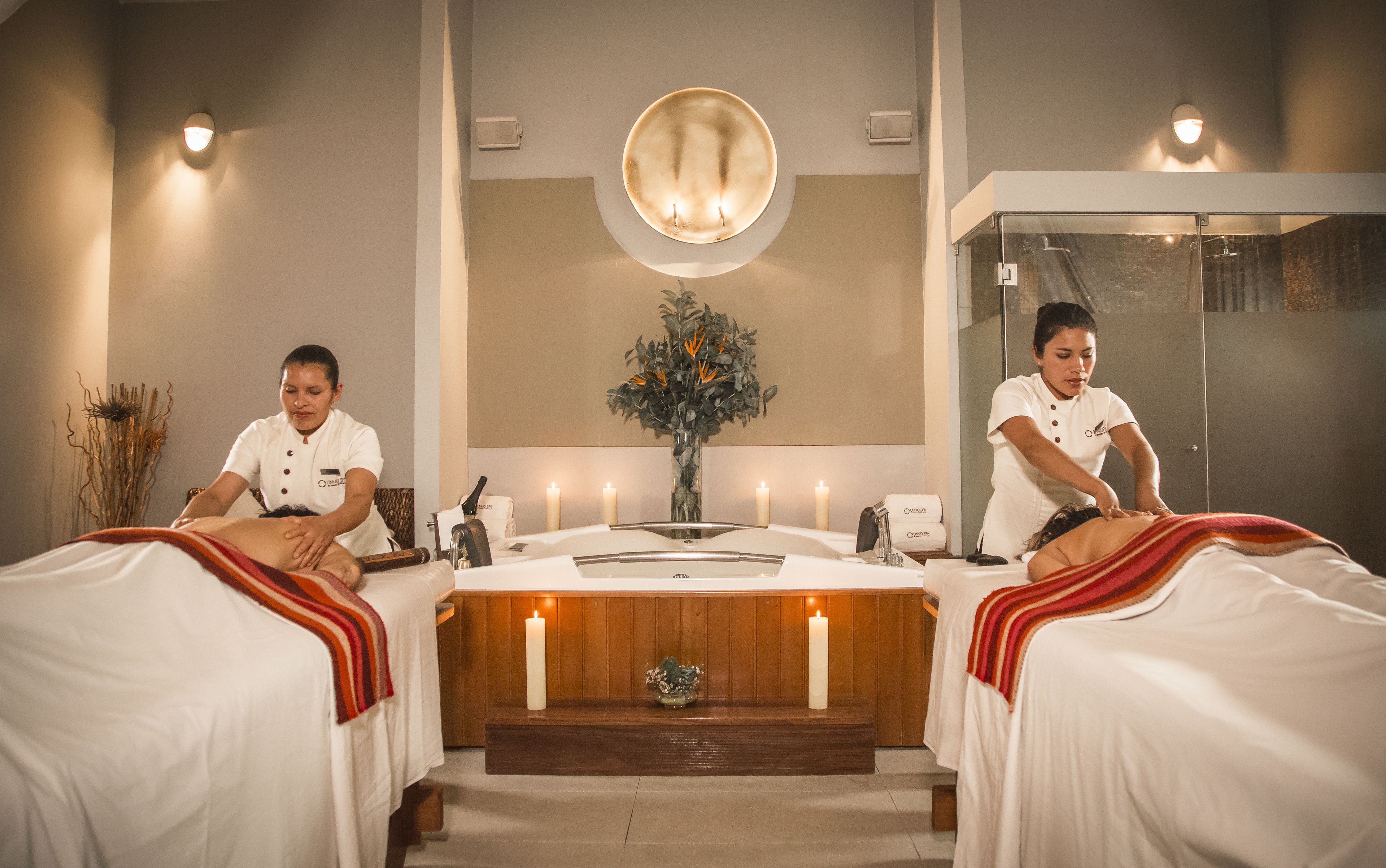 Un cuarto de spa con dos camas, una mesa central con velas y un espejo grande.