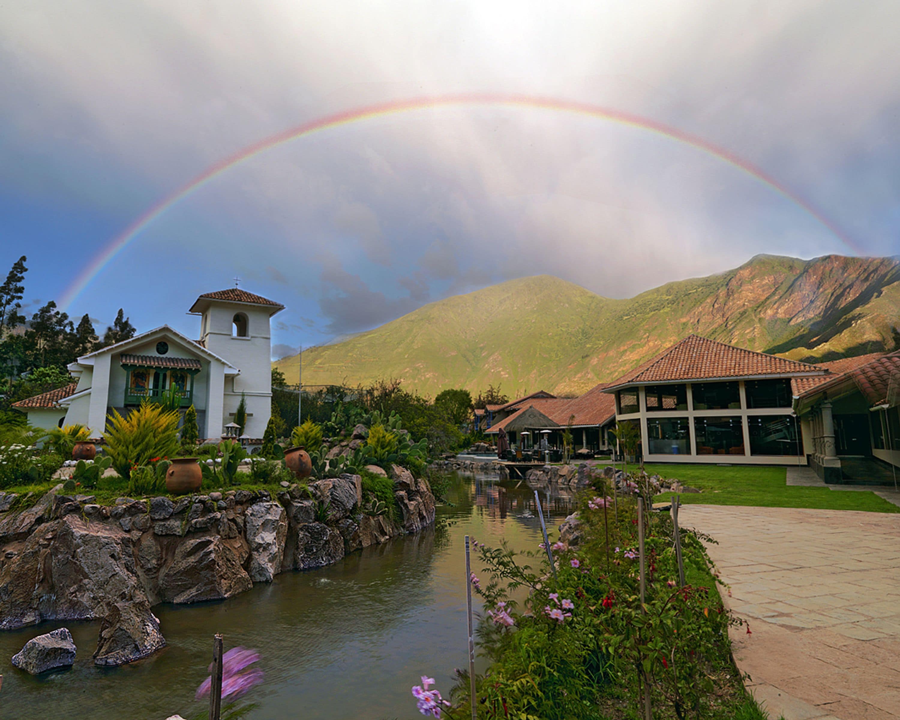 A resort with a river, a white building with a bell tower, and mountains in the background.