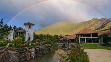A resort with a river, a white building with a bell tower, and mountains in the background.