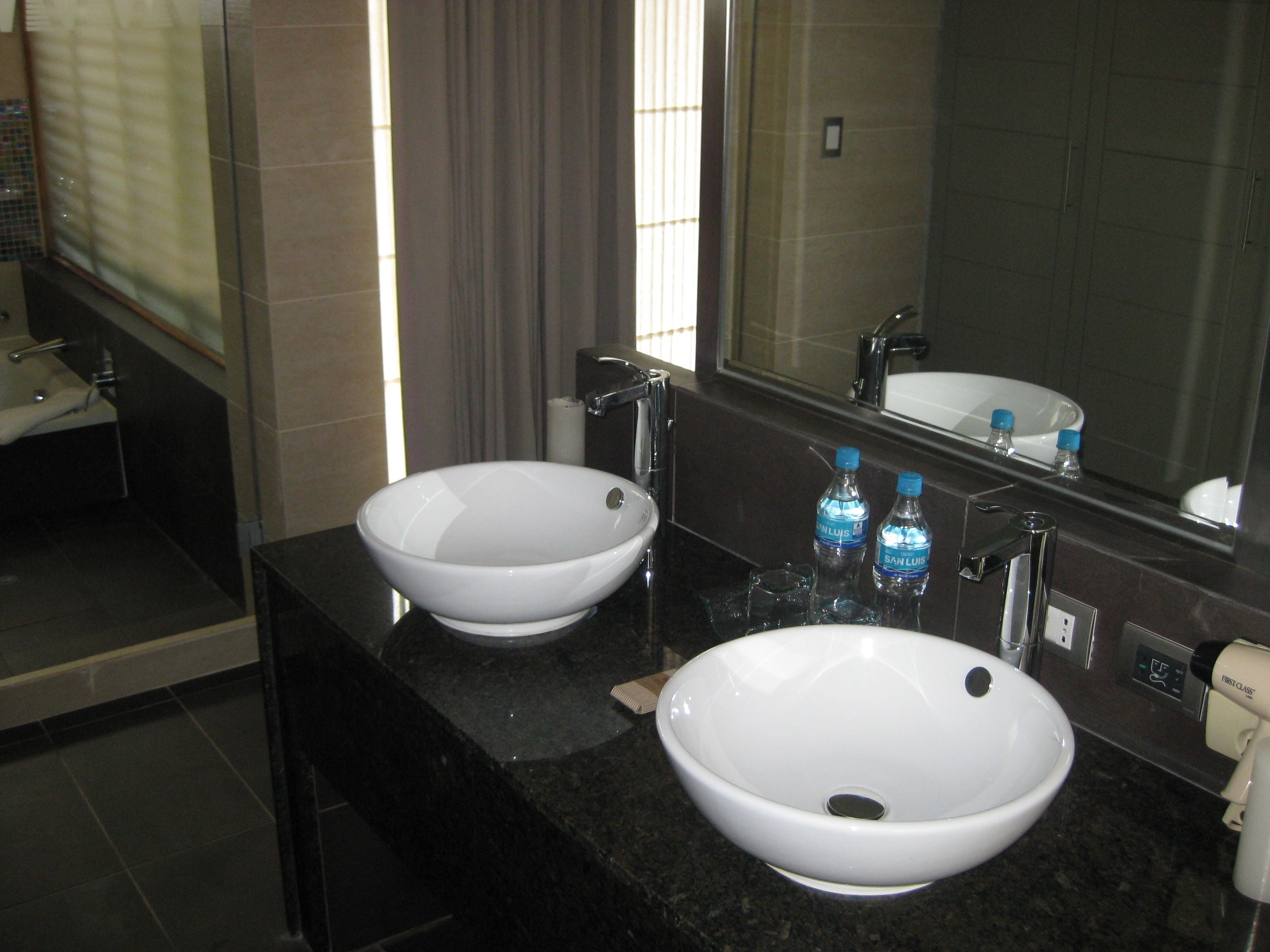 A bathroom with two white sinks, a mirror, and a shower.