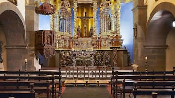 Interior de una iglesia con un altar ricamente decorado, bancales y una araña.