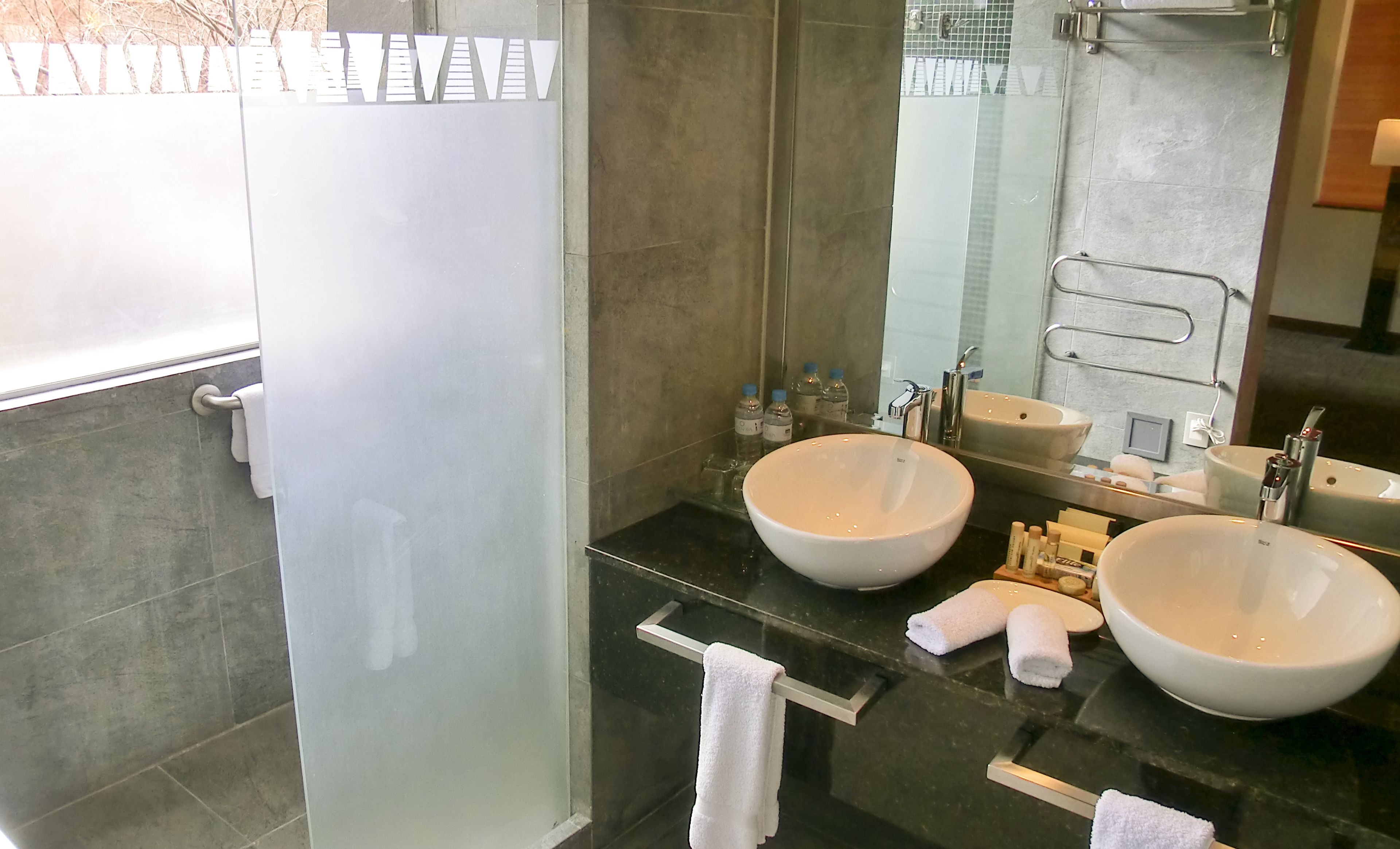 A modern bathroom with two large sinks, a glass shower enclosure, and a vanity with toiletries.
