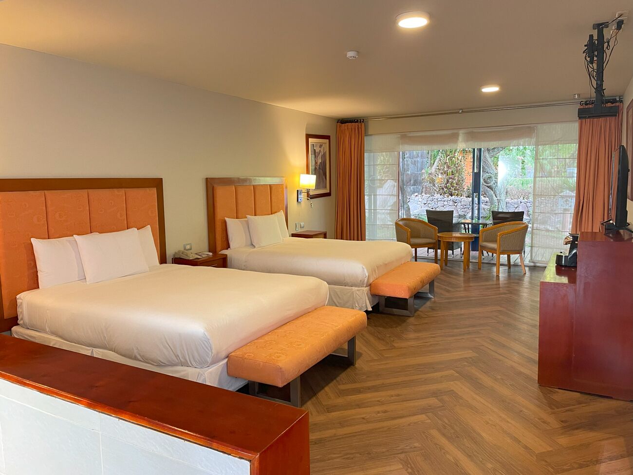 A hotel room with two beds, a desk, a chair, and a view of the outdoors.