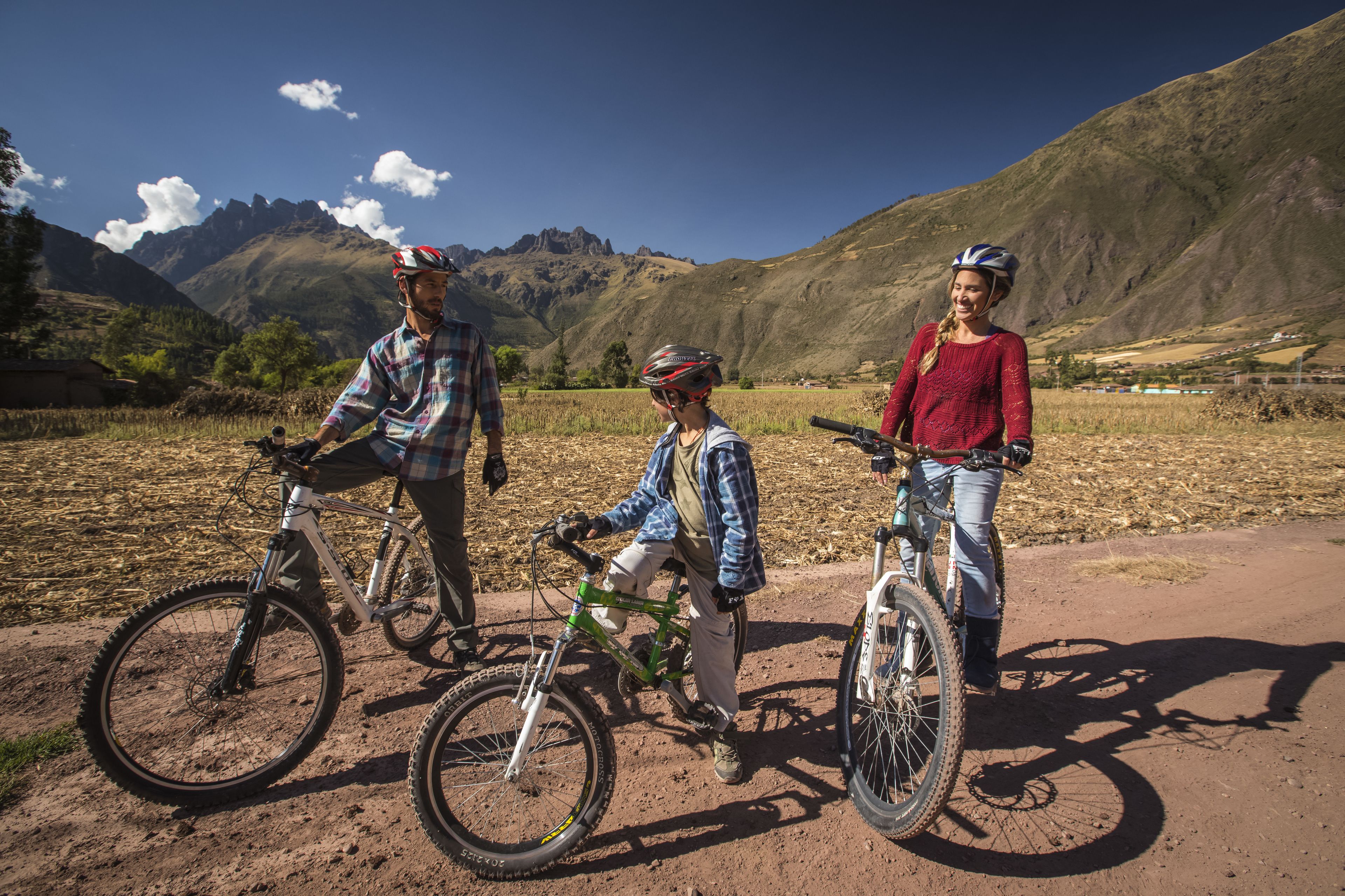 Three cyclists on a dirt path with mountains in the background.