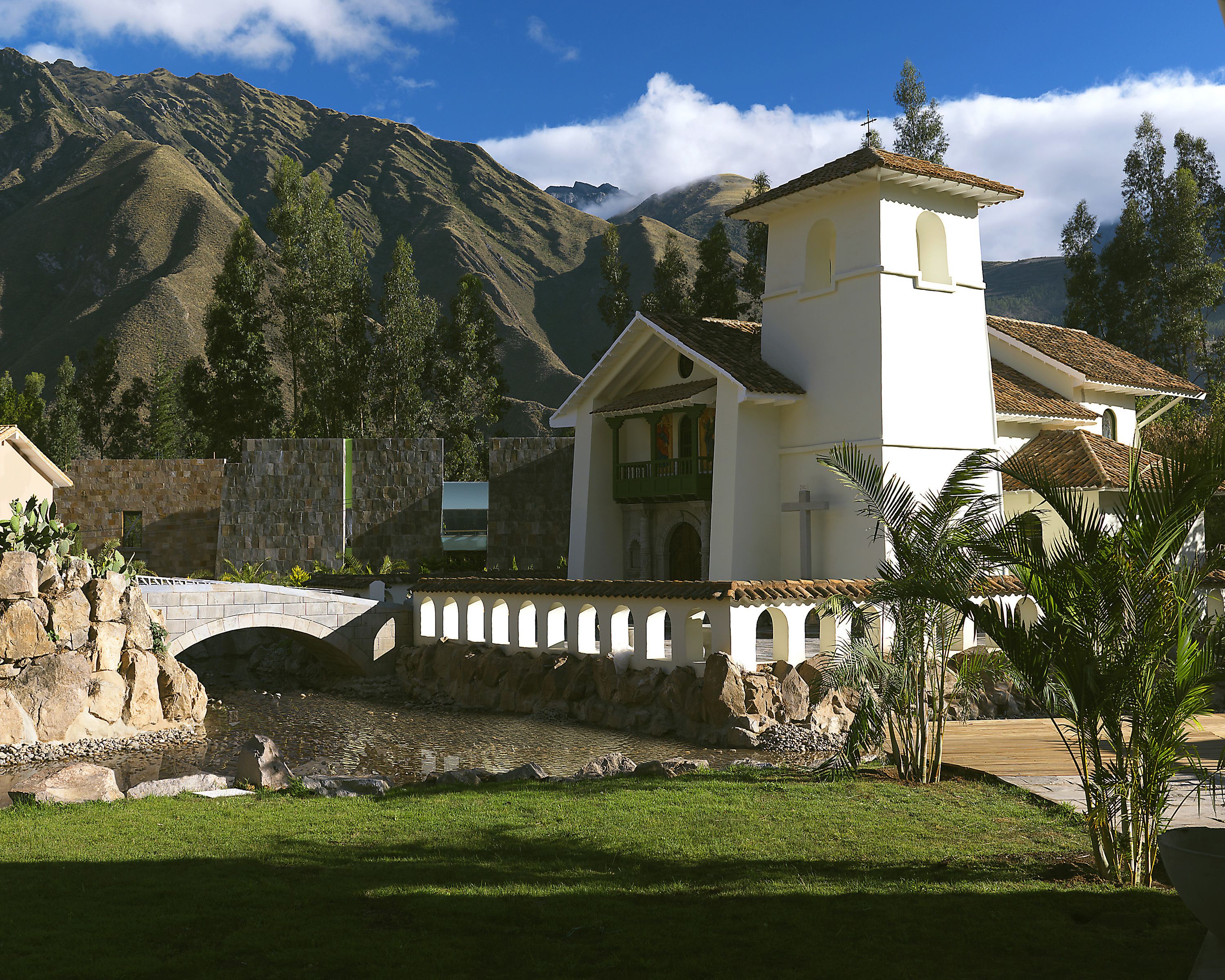 A white church with a bell tower, a stone bridge, and a mountain backdrop.