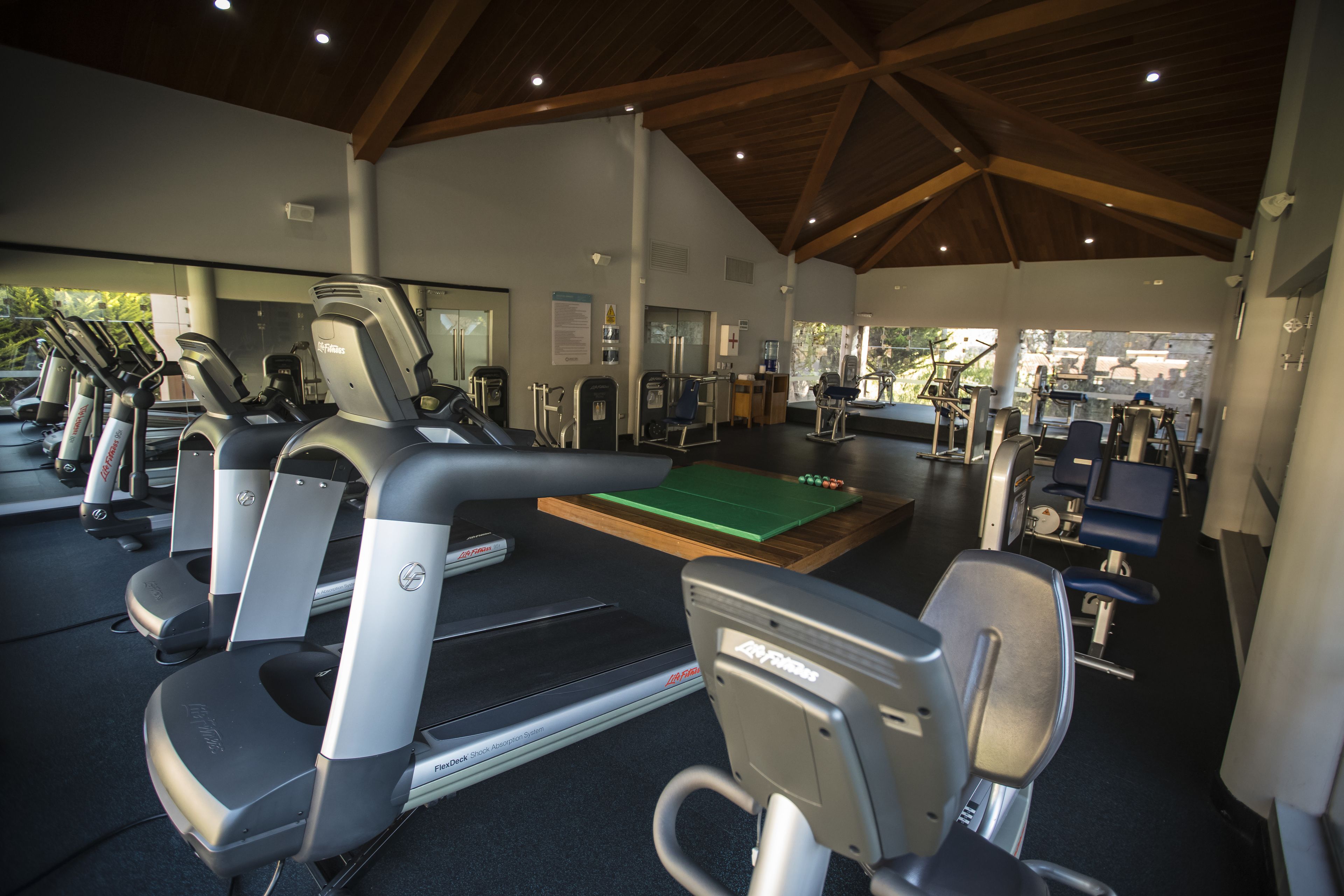 A gym with treadmills, elliptical machines, and a green exercise mat.