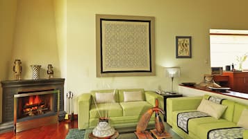 Una sala de estar con chimenea, sofás verdes, una mesa de centro y elementos decorativos.