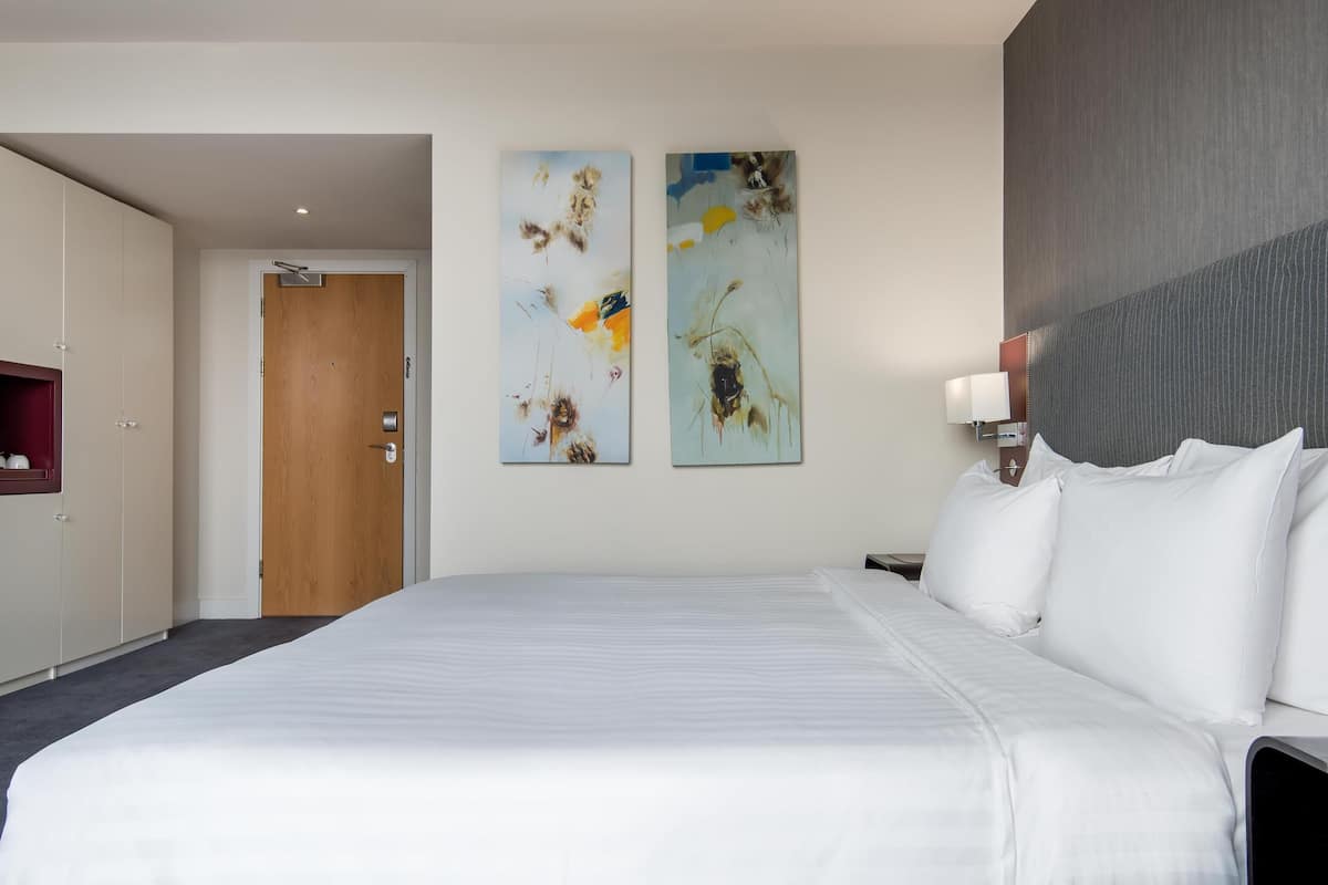 A hotel room with a large bed, a wardrobe, and two abstract paintings on the wall.