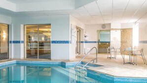 Una piscina interior con agua cristalina, un borde de azulejos y una zona de estar con sillas y una mesa.