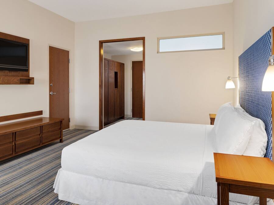 A hotel room with a large bed, a wooden dresser, a television mounted on the wall, and a small table.