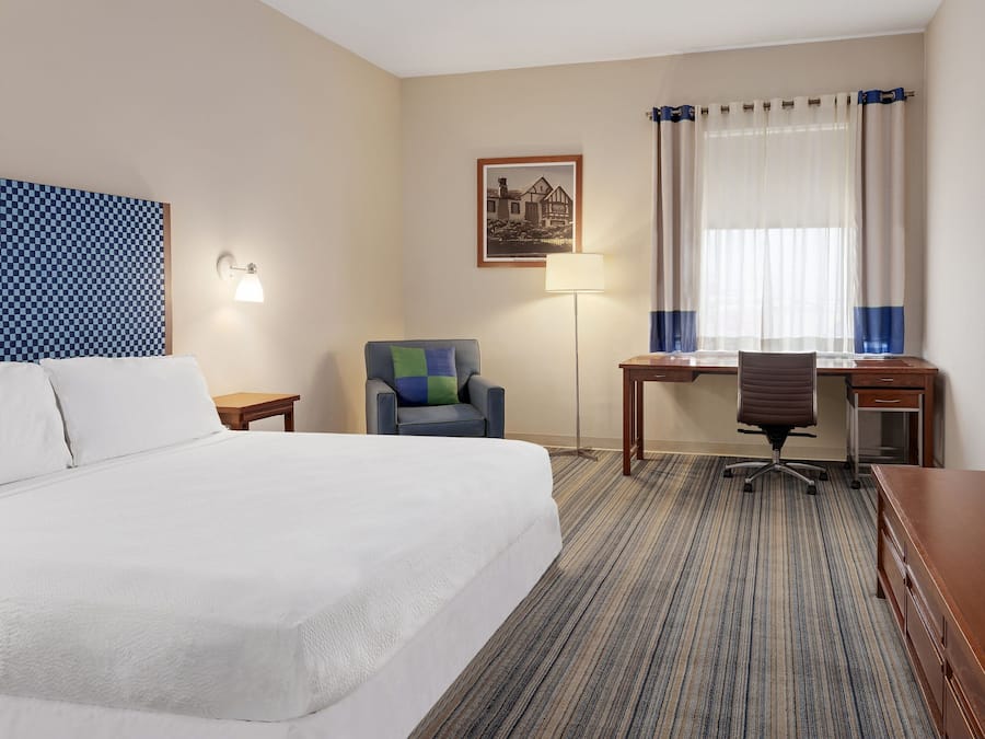 A hotel room with a large bed, a desk, a chair, a lamp, and a window with curtains.