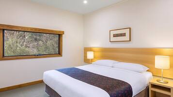 A hotel room with a large bed, a window with a view of trees, a bedside table with a lamp, and a framed picture on the wall.