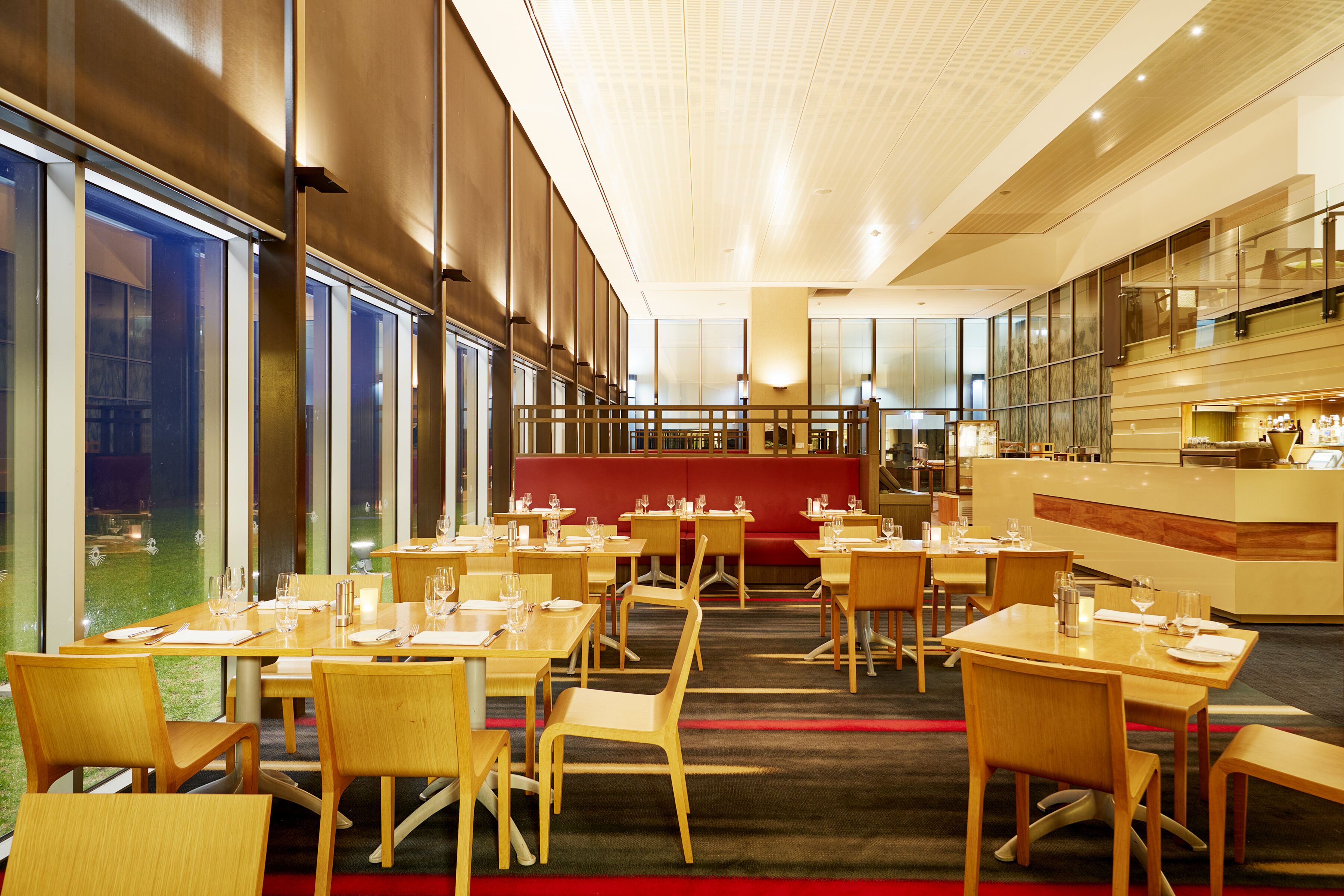 A modern restaurant with wooden tables and chairs, a red seating area, and a bar counter.