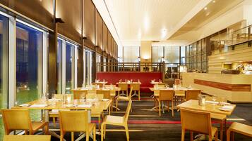 A modern restaurant with wooden tables and chairs, a red seating area, and a bar counter.