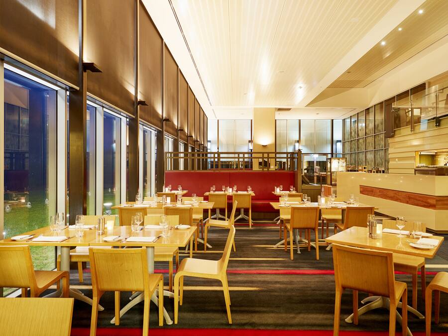 A modern restaurant with wooden tables and chairs, a red seating area, and a bar counter.
