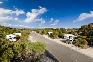 Un campament amb autocaravanes estacionades al costat d'un camí, envoltat de verdura i arbres.