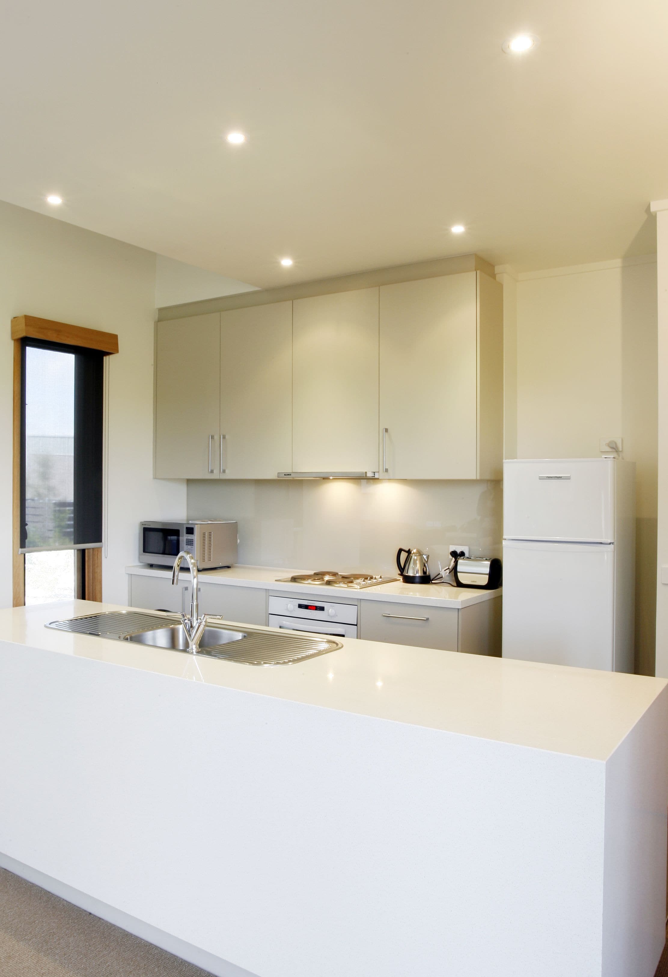 A modern kitchen with white cabinetry, a stainless steel sink, a microwave, a toaster, and a refrigerator.