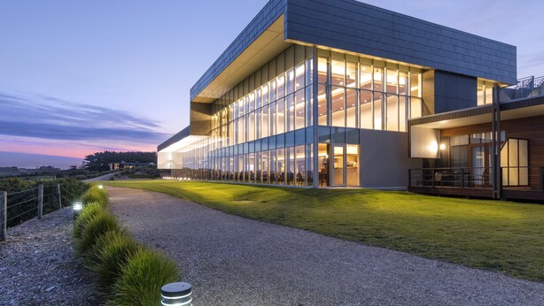 Un bâtiment moderne doté de grandes fenêtres en verre et d’un chemin de gravier menant à l’entrée.