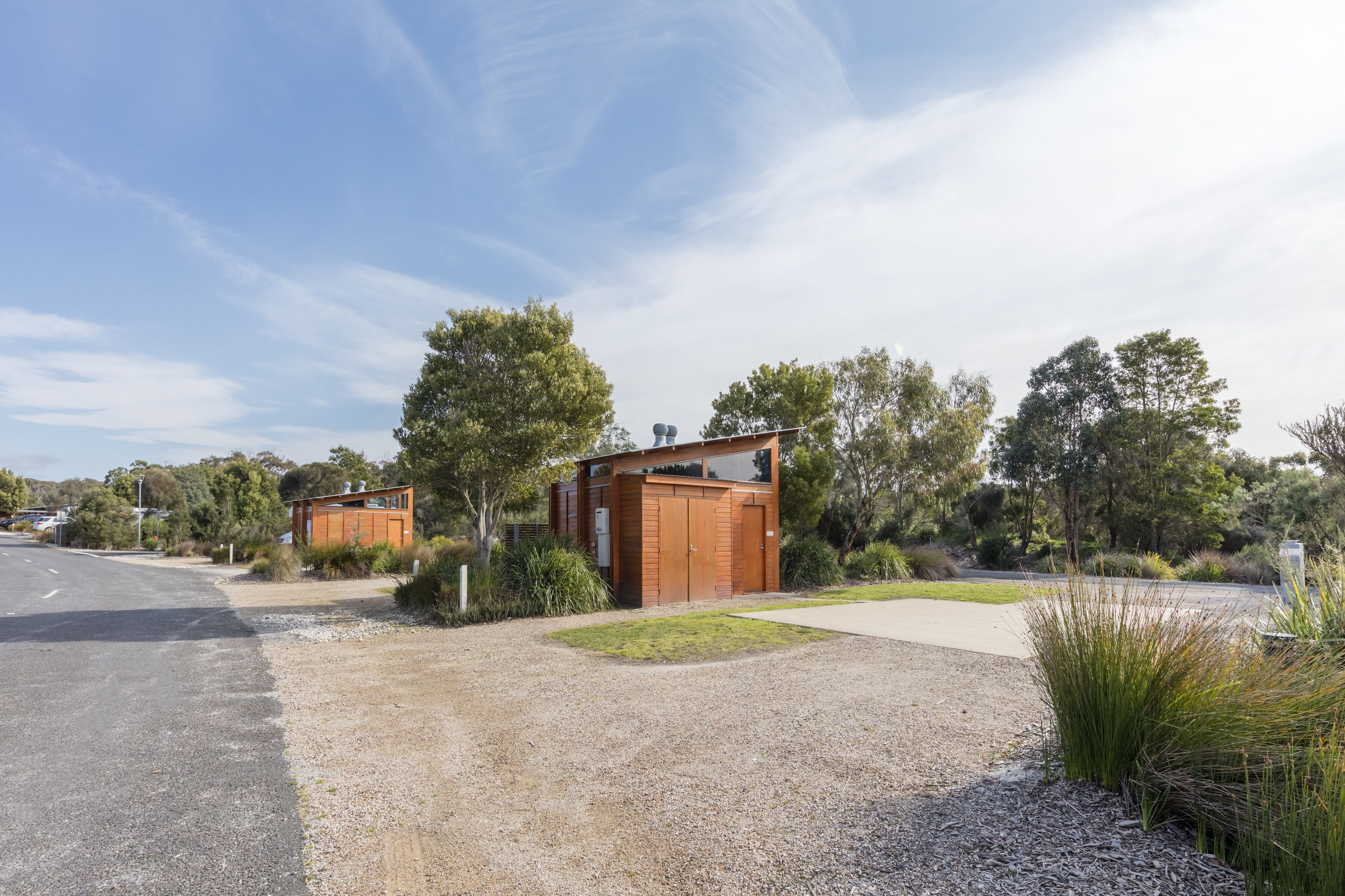 A modern building with a large garage door, surrounded by gravel and grass, with trees and a clear sky in the background.