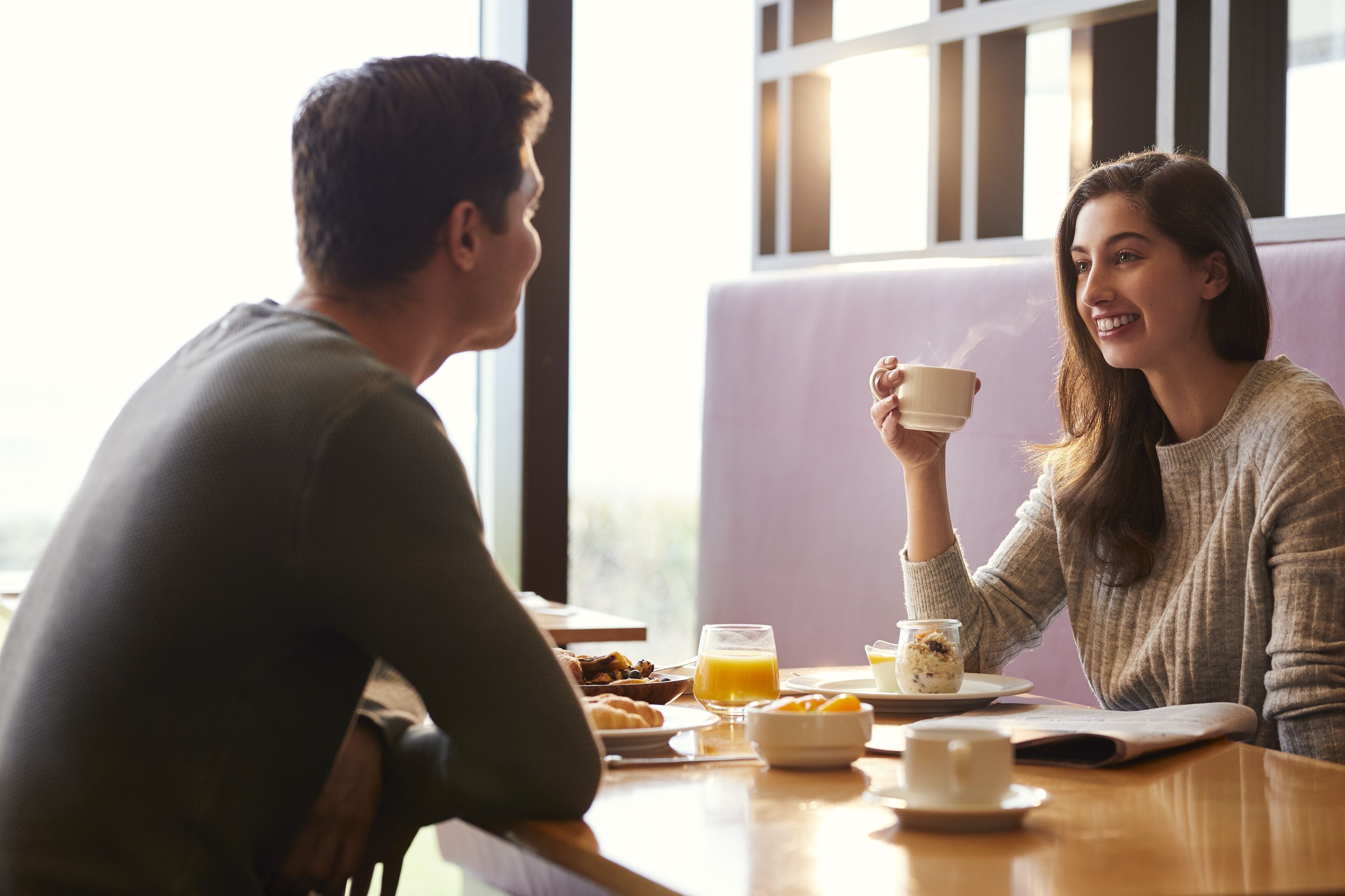 Une table à manger avec des aliments pour le petit-déjeuner, une tasse de café et une personne tenant une tasse.
