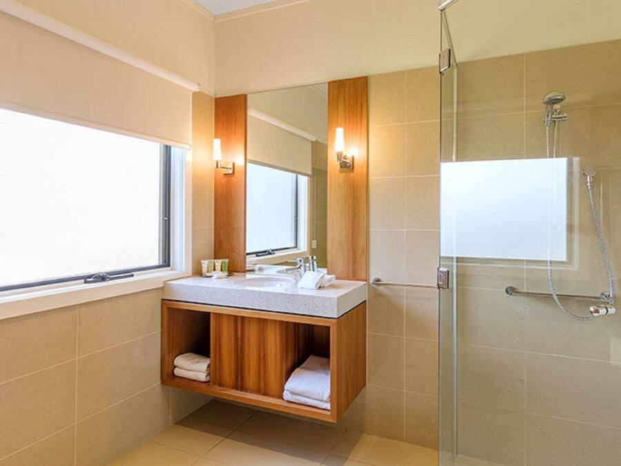 Un baño moderno con un ventanal grande, cabina de ducha de vidrio y tocador de madera con espejo.