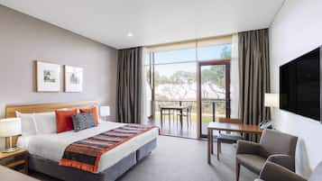 Habitación de hotel con una cama grande, un escritorio, una silla y un balcón con mesa y sillas.