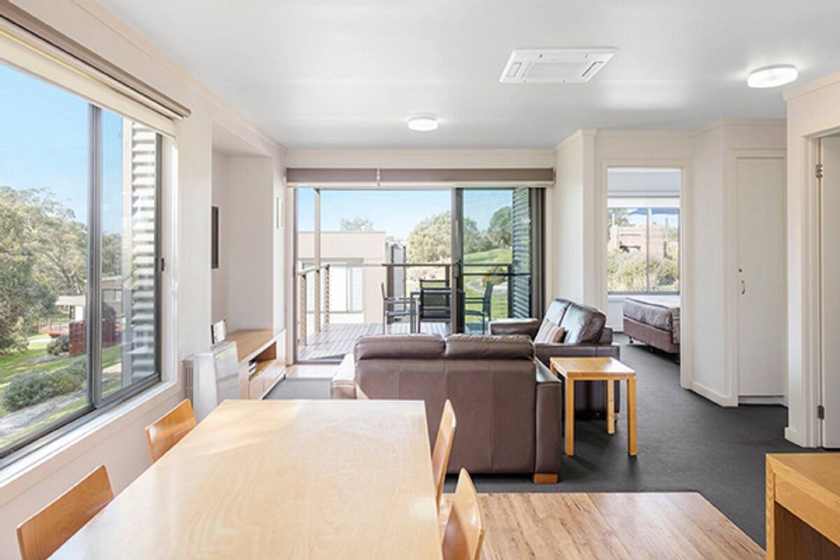 A spacious living area with a large dining table, a sofa, and a balcony with a view of the outdoors.