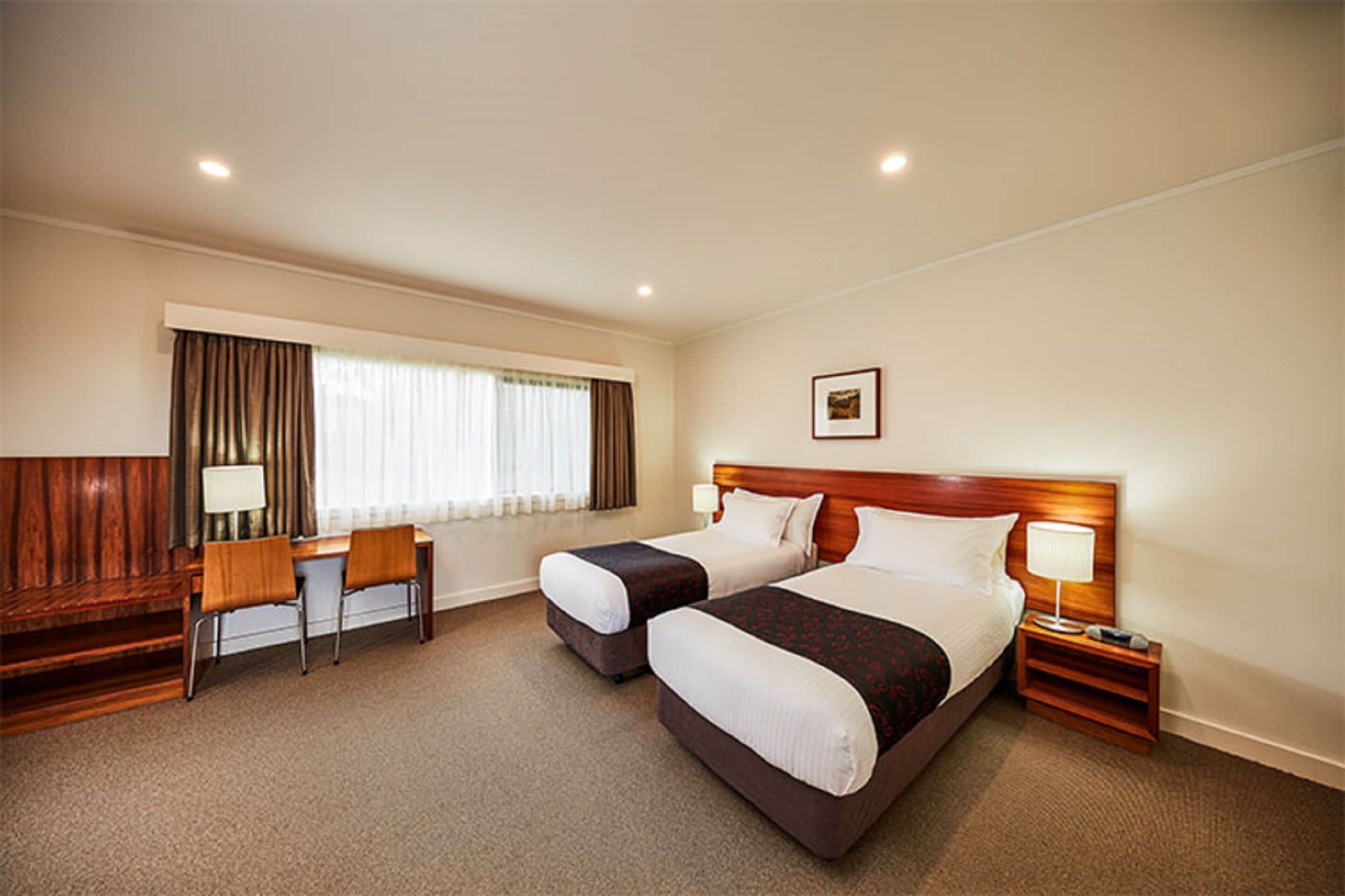Habitación de hotel con dos camas, un escritorio, sillas y una ventana con cortinas.