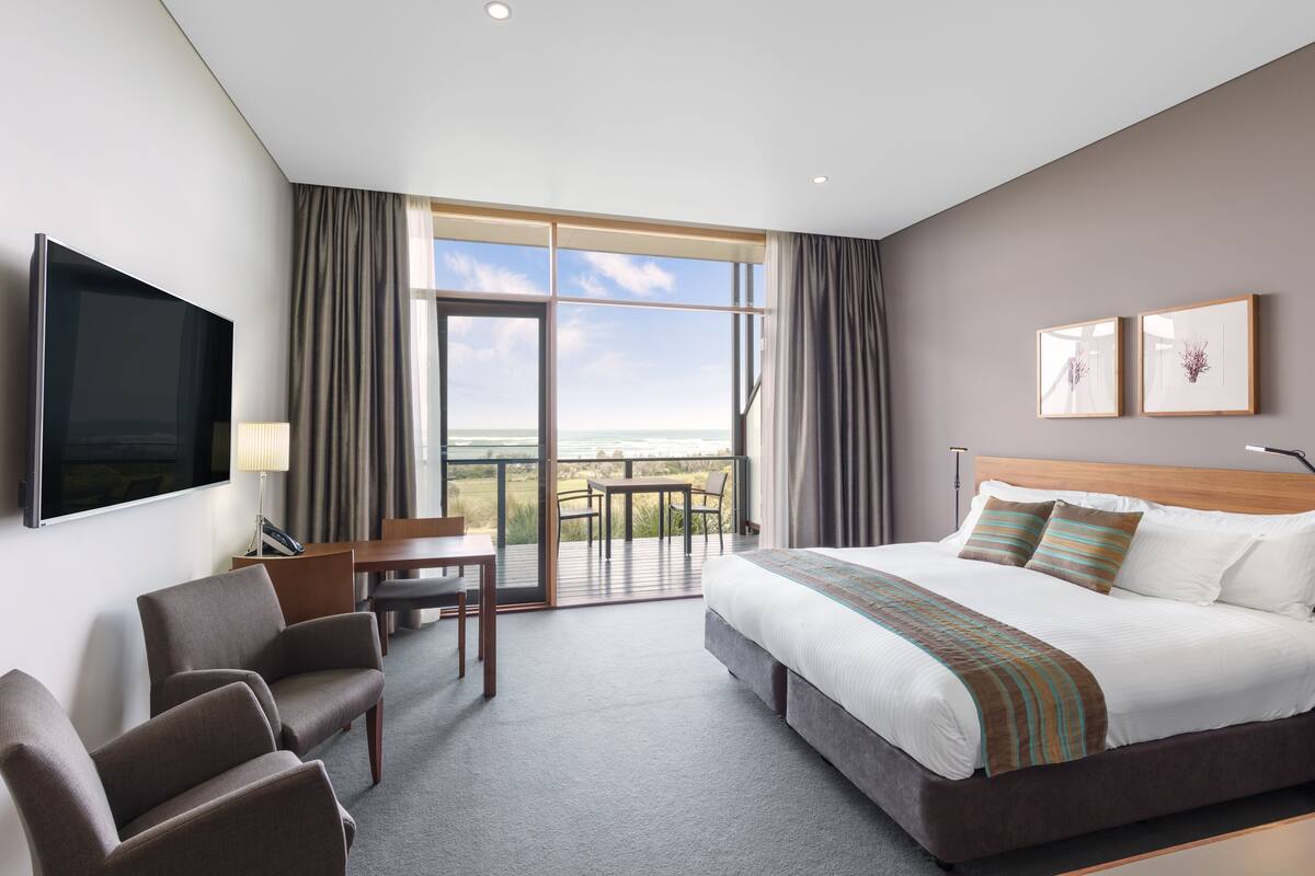 A hotel room with a large bed, a TV, a desk, and a balcony with a view.