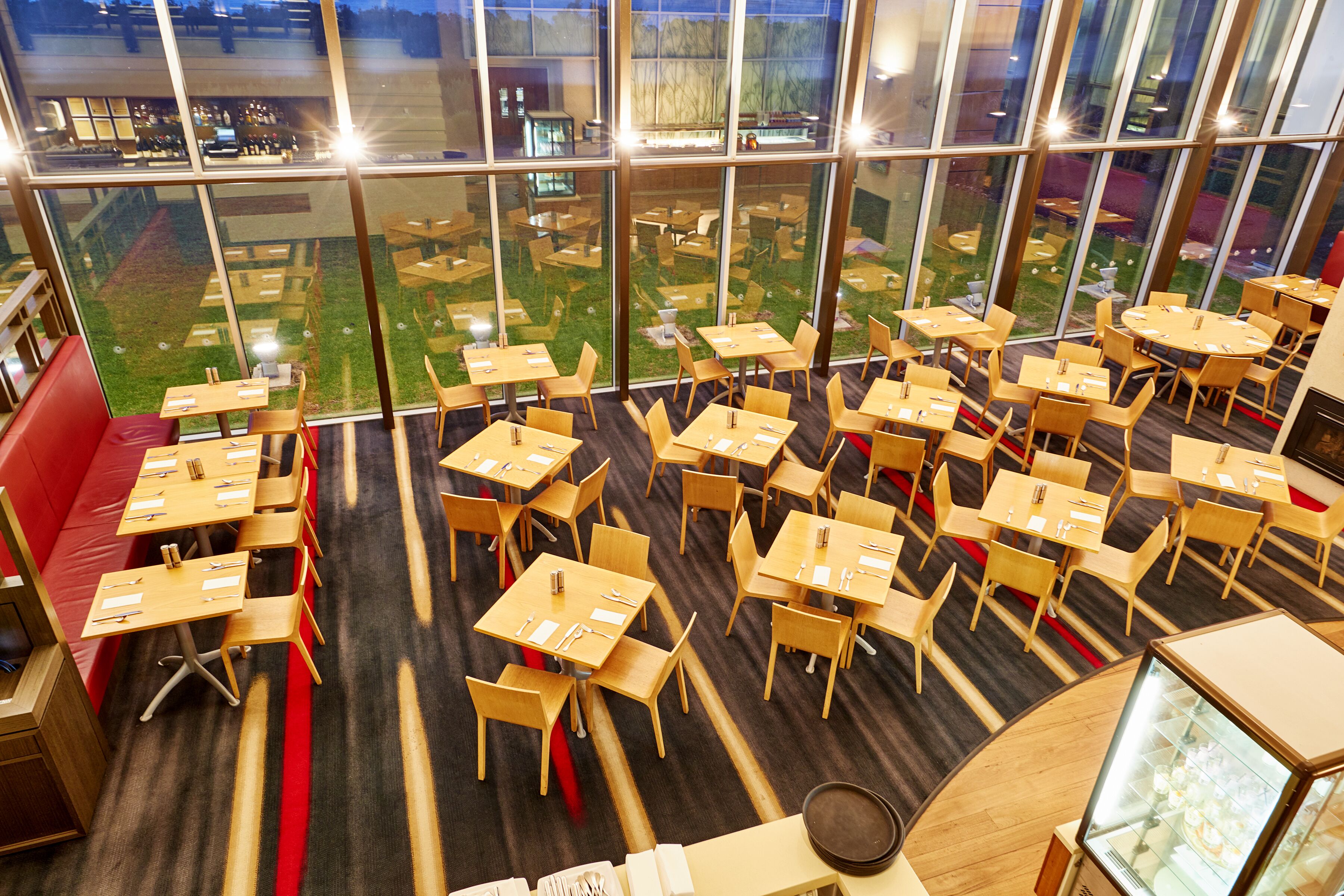 A spacious restaurant with multiple tables and chairs, large windows offering a view of the outdoor area, and a modern interior design.