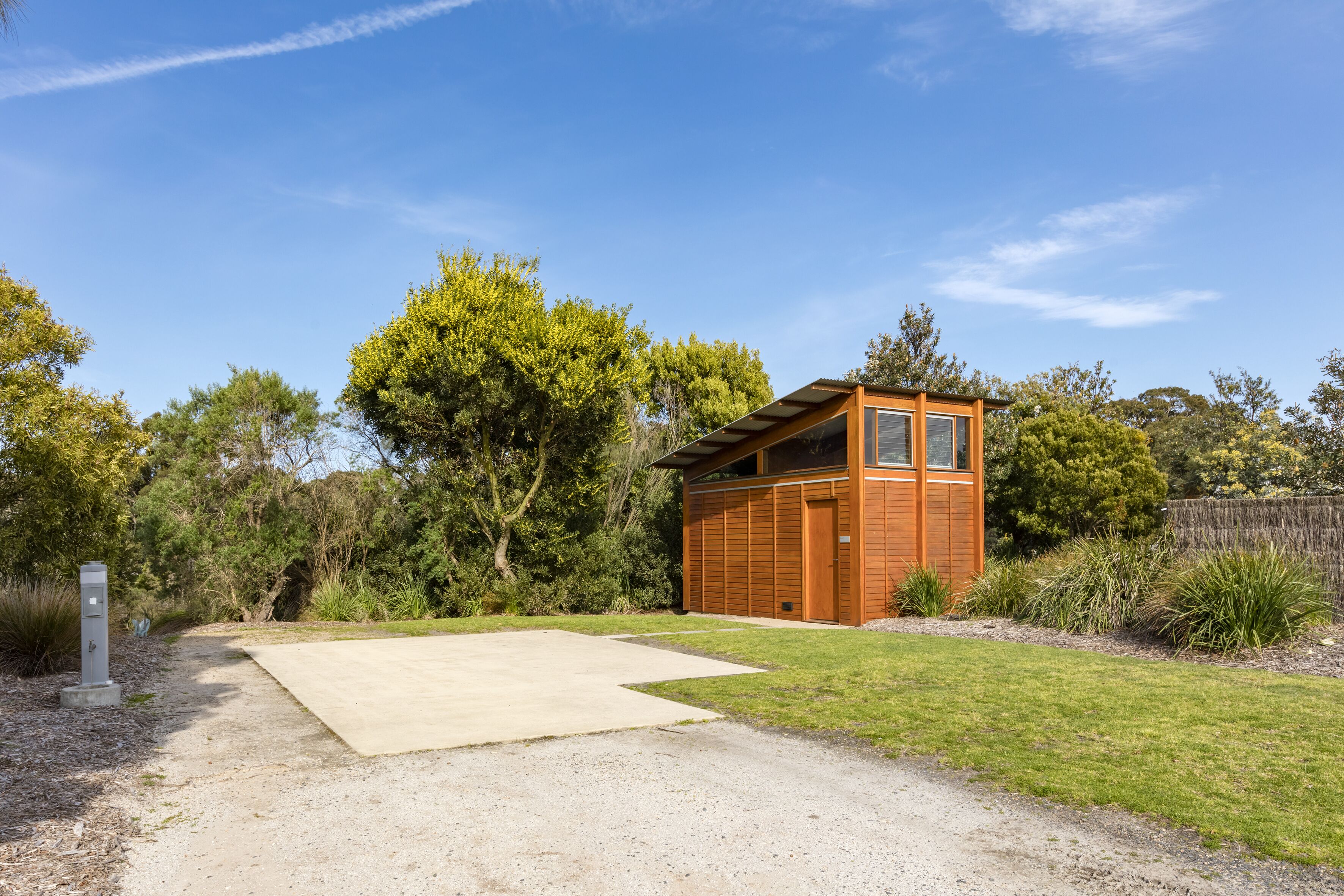A small, single-story wooden cabin with a garage, surrounded by a well-maintained lawn and dense trees.