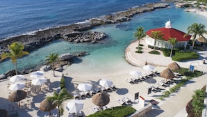 A beach resort with a clear view of the ocean, a rocky shoreline, and a building with a red roof.