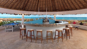 A bar area with a pool table, bar stools, and a view of the ocean.