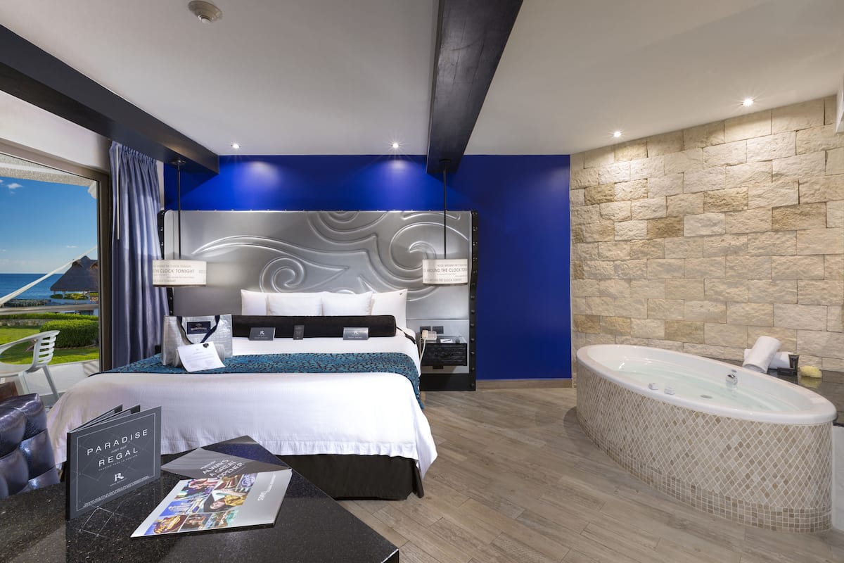 A modern hotel room with a large bed, a separate bathroom with a jacuzzi, and a view of the sea.