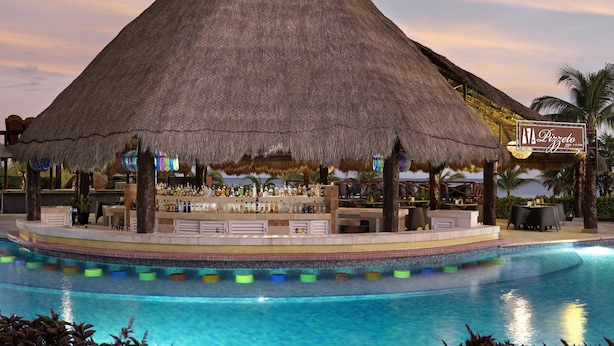 A bar area with a thatched roof, poolside seating, and a sign for 'Pizzeria'.