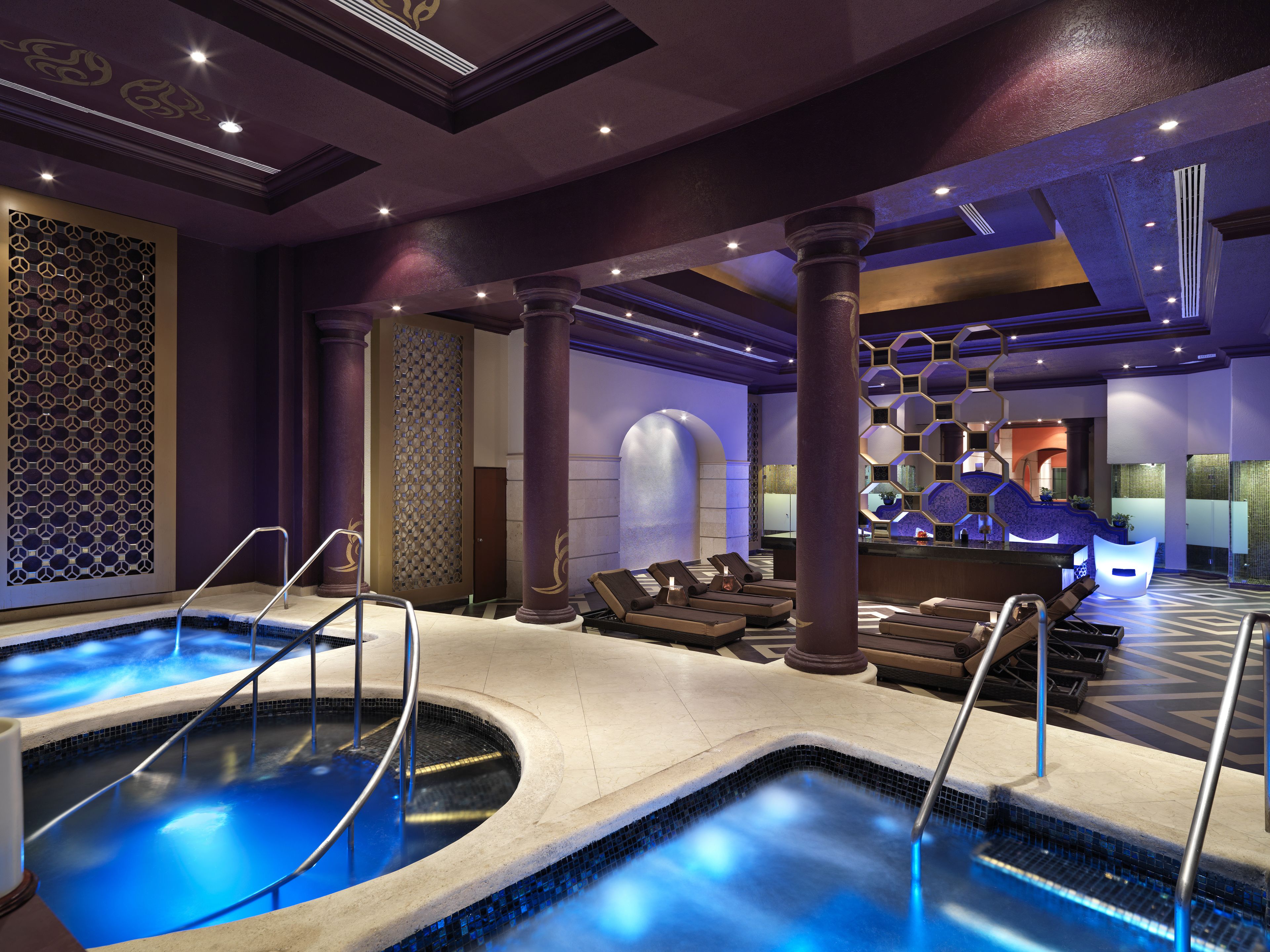 A spa area with two hot tubs, a reception desk, and a decorative wall with geometric patterns.